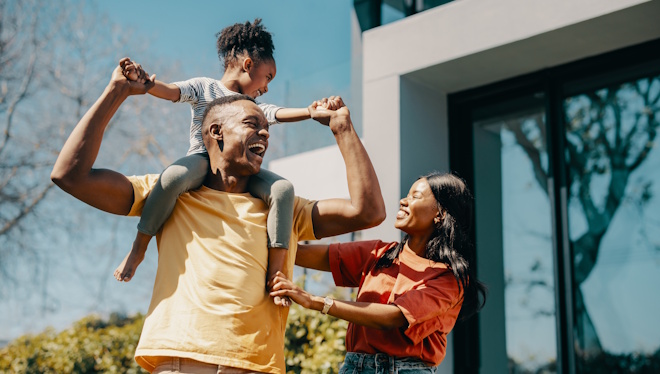Family fun time with mom and dad at home. Couple playing with their daughter and creating happy childhood memories. Dad carrying his daughter on his shoulders and standing next to mom.
