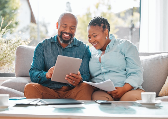 A man and woman seated on a couch, smiling and looking at some papers.