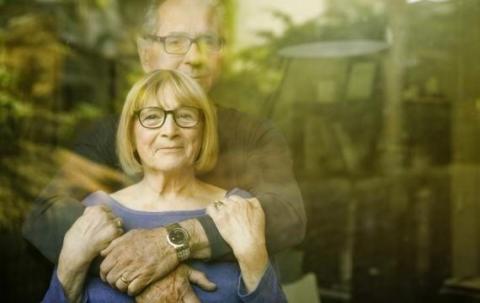 A man and woman holding each other while looking through a window.