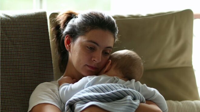A woman holding a young baby while sitting on a couch.