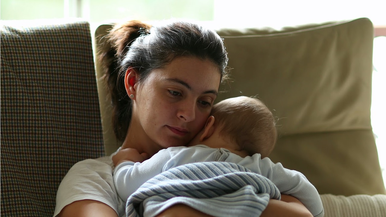 A woman holding a young baby while sitting on a couch.