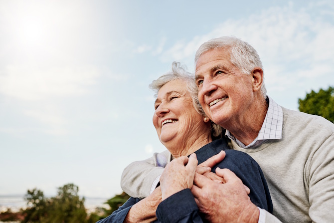 An elderly man and woman outside hugging.