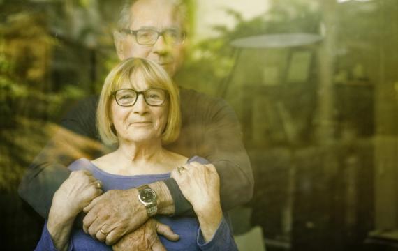 A man and woman holding each other while looking through a window.
