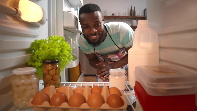 A man looking in a fridge at a variety of food